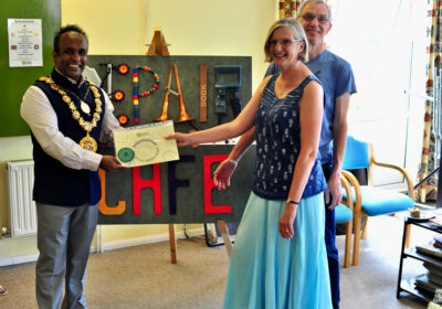 Atiqul Hoque presents a commemorative certificate and handcrafted badge to SRCs 1000th visitor, Christine Taylor with husband Richard looking on
