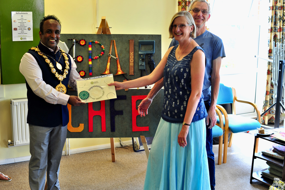 Atiqul Hoque presents a commemorative certificate and handcrafted badge to SRCs 1000th visitor, Christine Taylor with husband Richard looking on